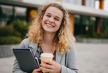 Woman holding notebook and coffee smiling for the camera